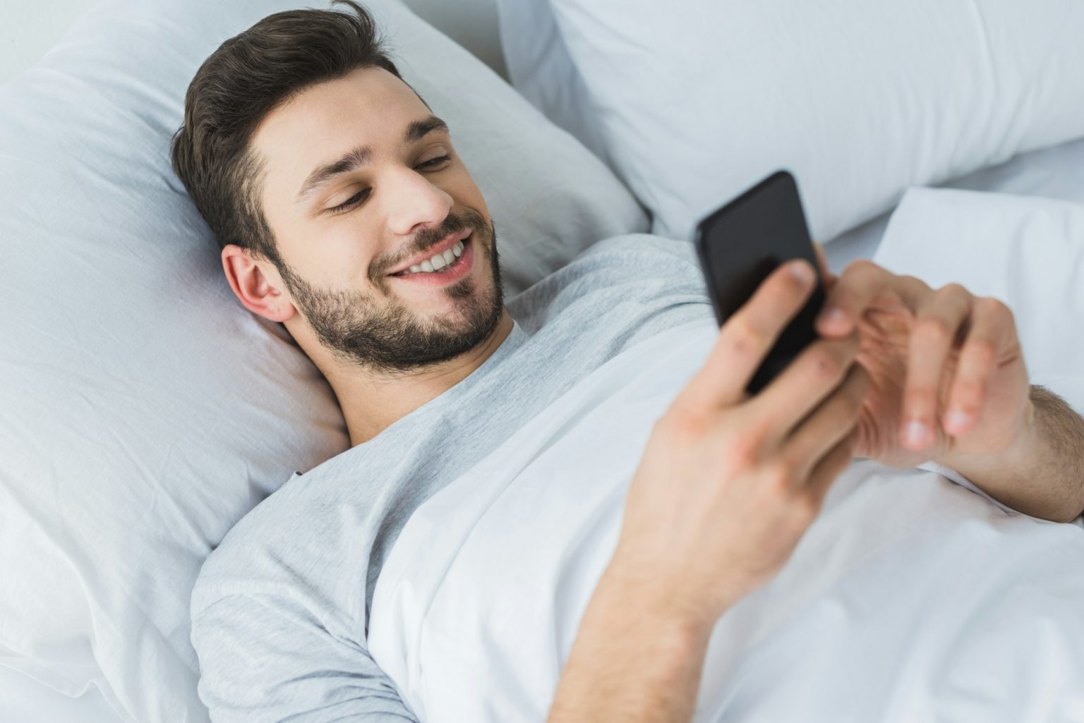 Comment rendre amoureux un homme qui veut juste coucher ? happy bearded man using smartphone in bed in the morning